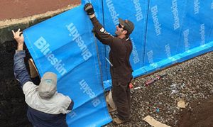 Aquatight crew installing foundation waterproofing on home